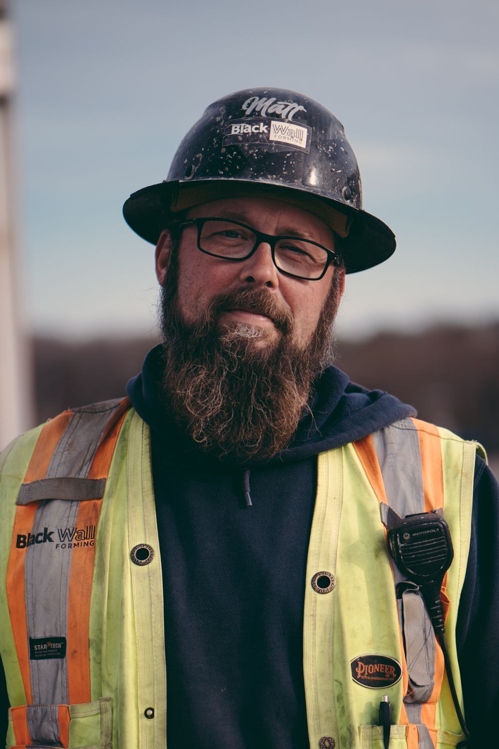 Man in hard hat, glasses, and safety vest standing outdoors at a worksite