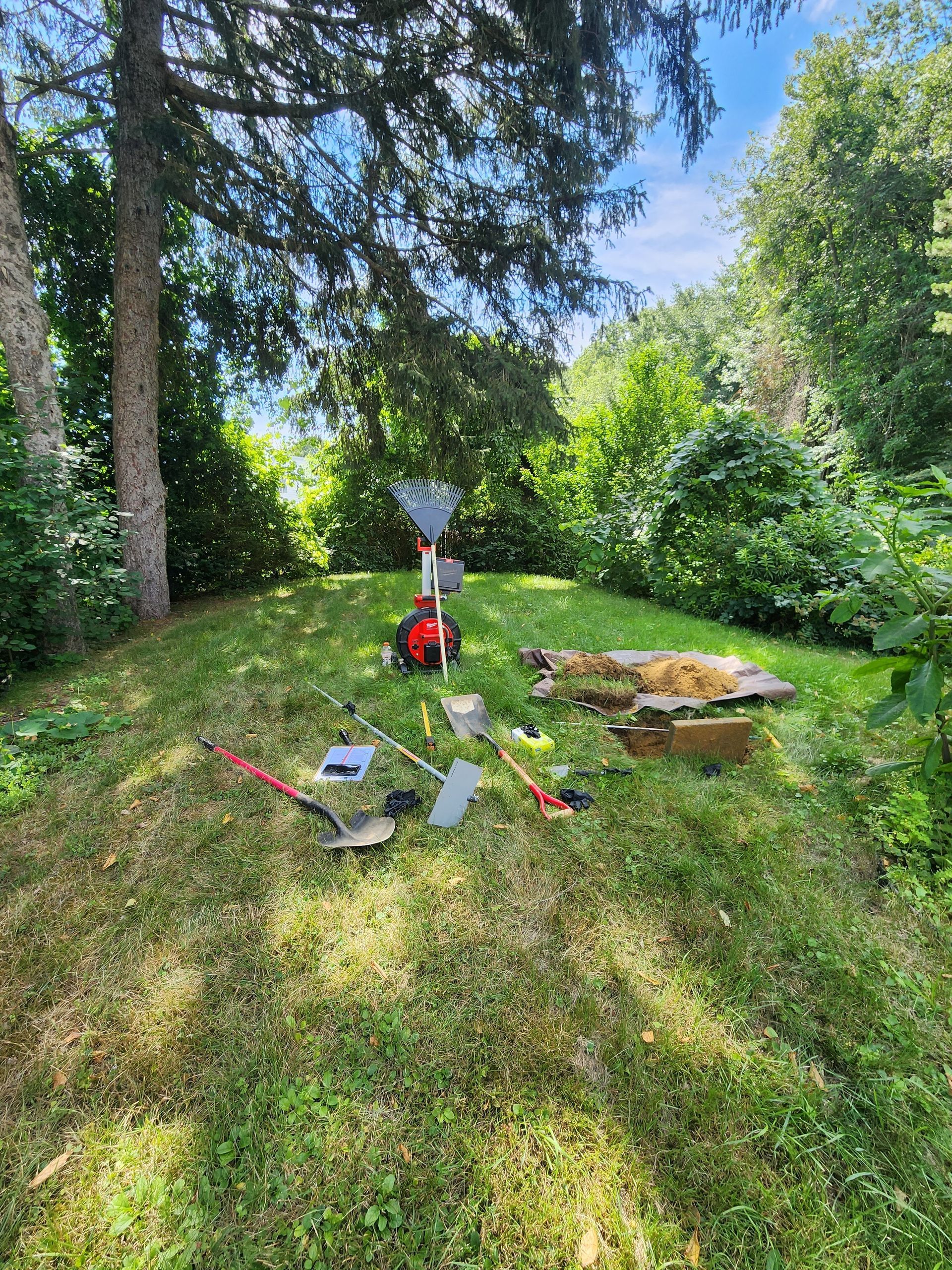 Outdoor lawn with a red machine, tools, and a table in a sunny garden under trees