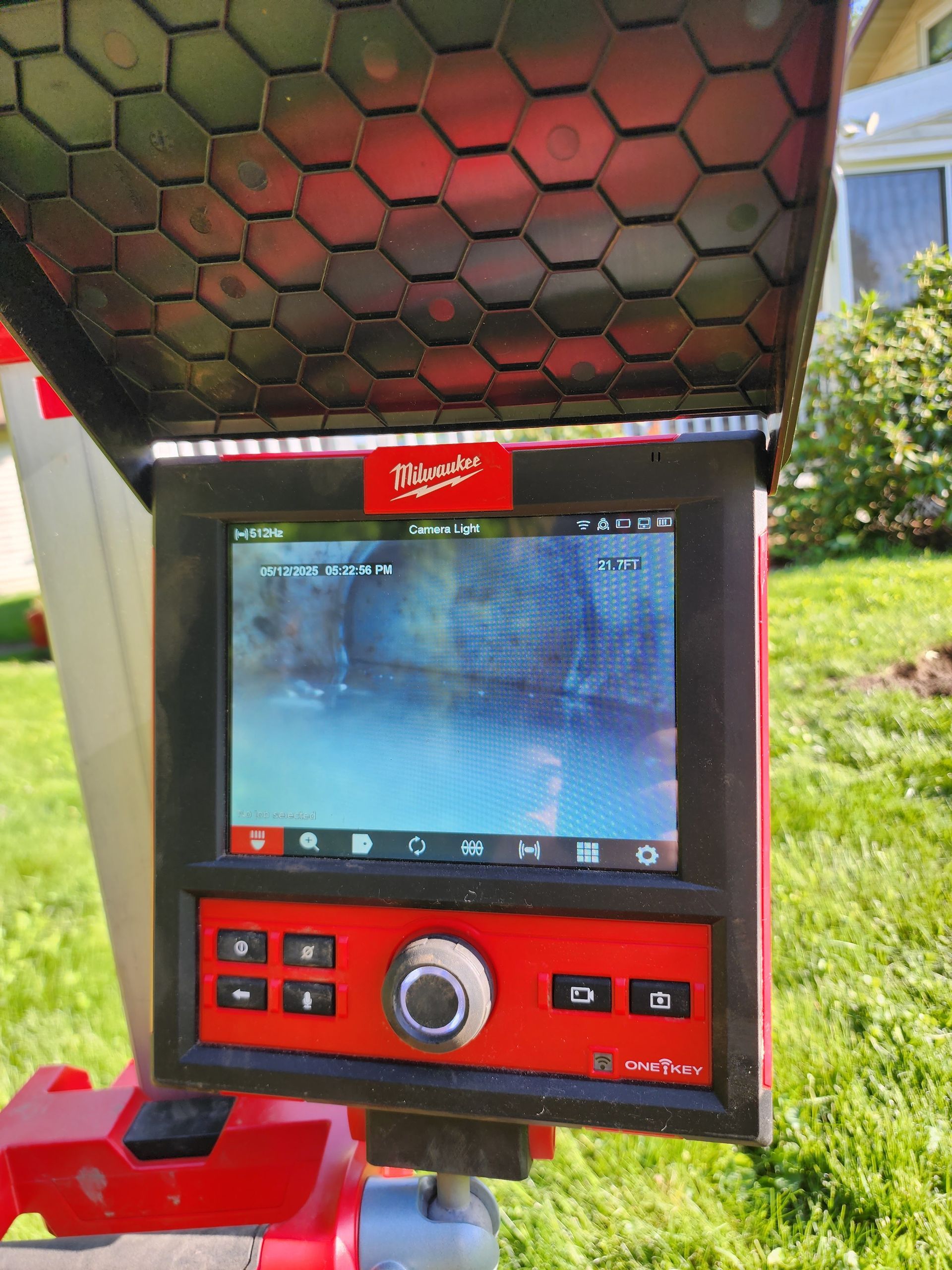 Red handheld diagnostic device with screen and control buttons on a lawn outdoors