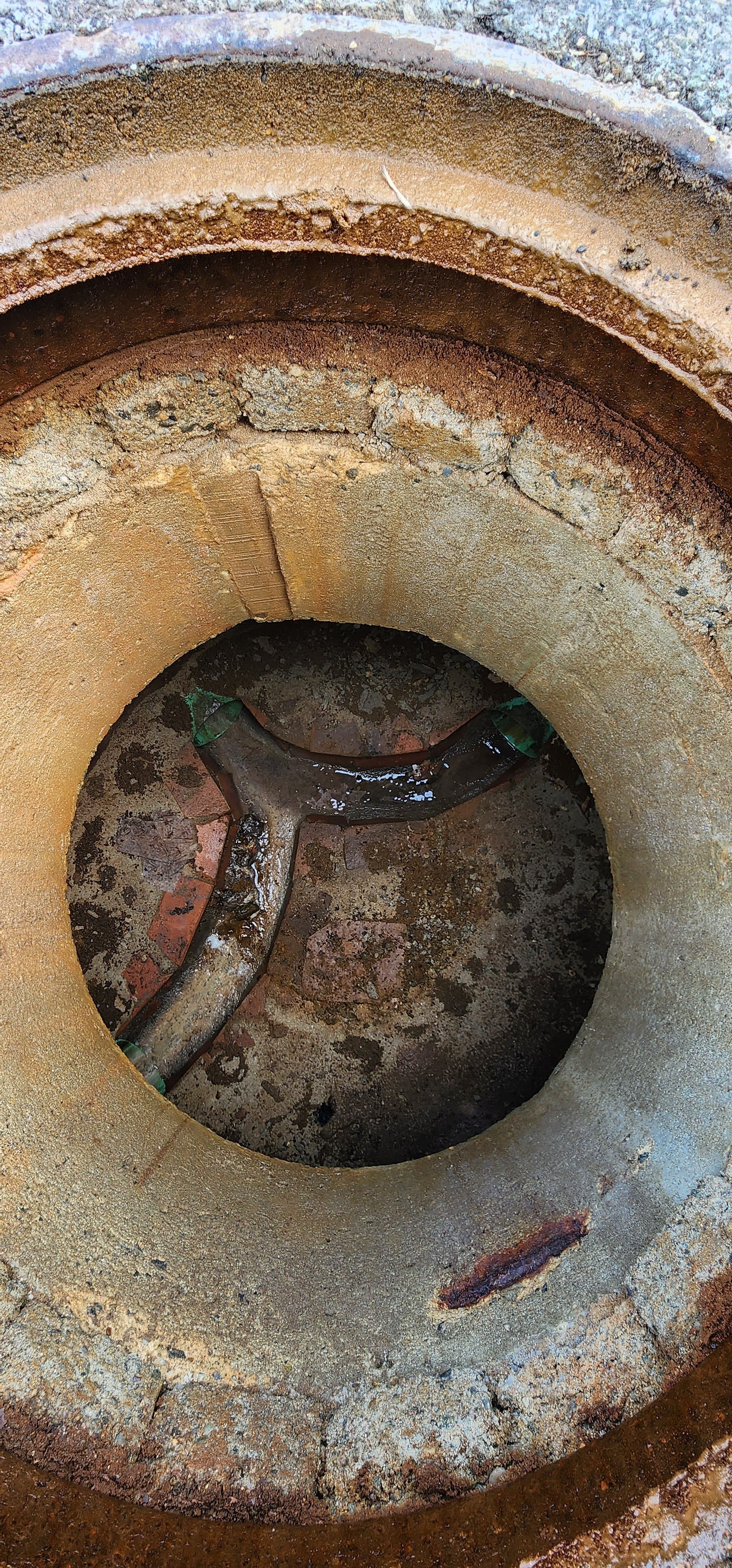 Close-up of a rusty metal drain opening with a circular concrete rim and dark debris inside