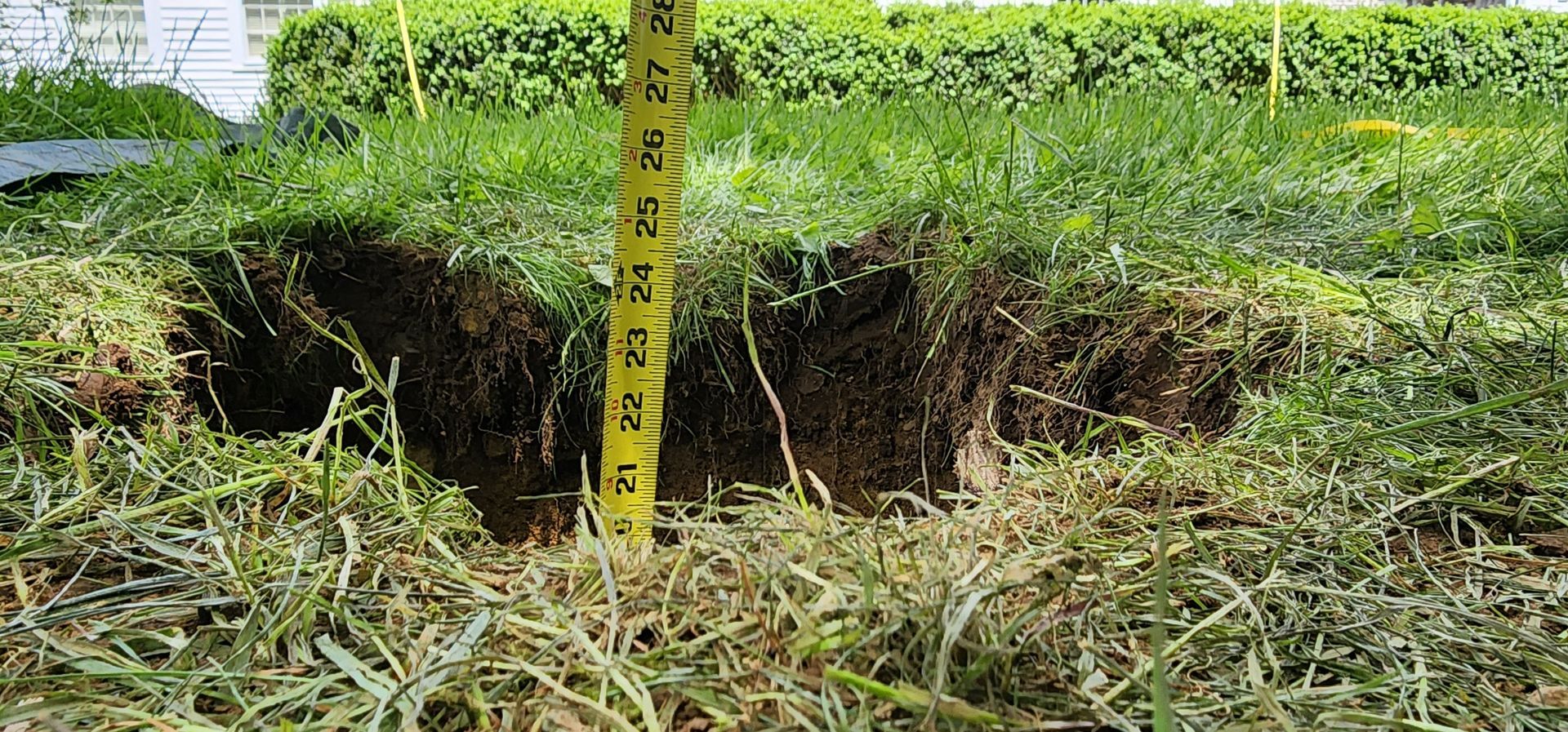 Freshly dug hole in grassy field with a yellow measuring tape standing in the center