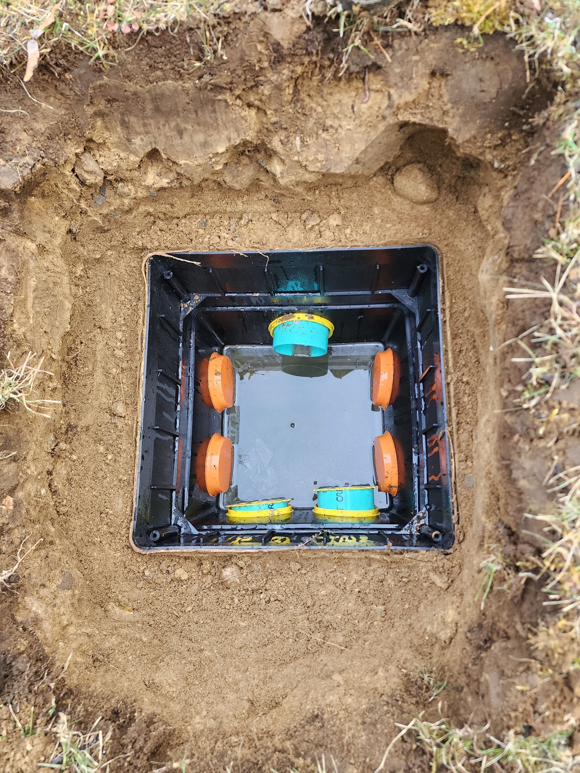 Square black utility box in a dirt hole, with orange and blue components inside.