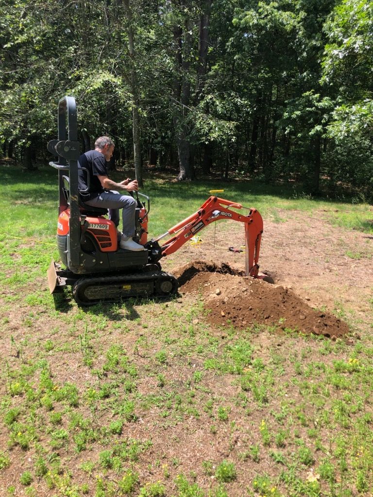 Compact excavator digging dirt in a grassy yard near trees