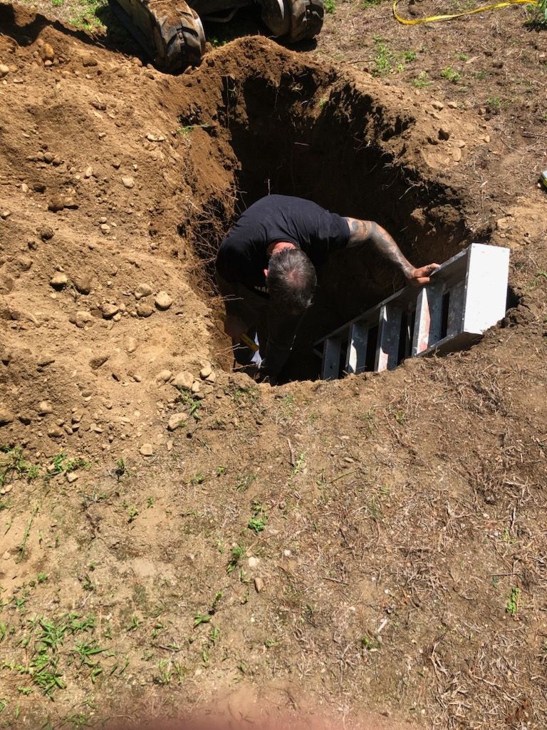 Person climbing into a small dirt pit with a white panel or barrier at the entrance outdoors.
