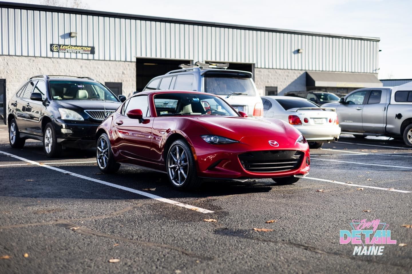 Red Mazda Miata convertible parked outside a building, surrounded by other vehicles.