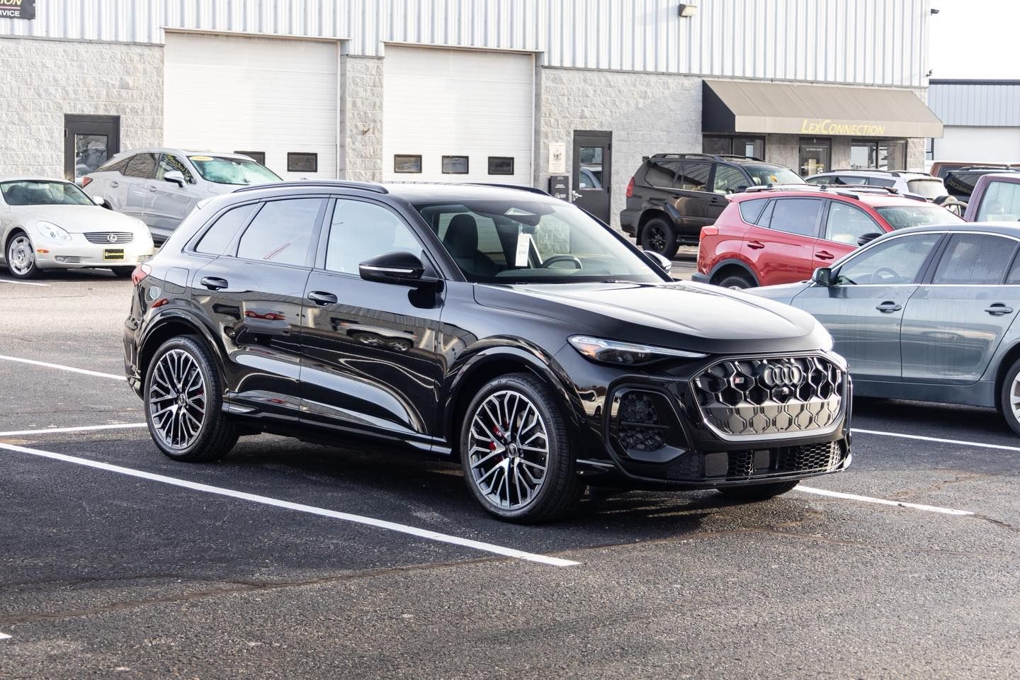 Black Audi SUV parked in a lot with other vehicles and a building in the background.