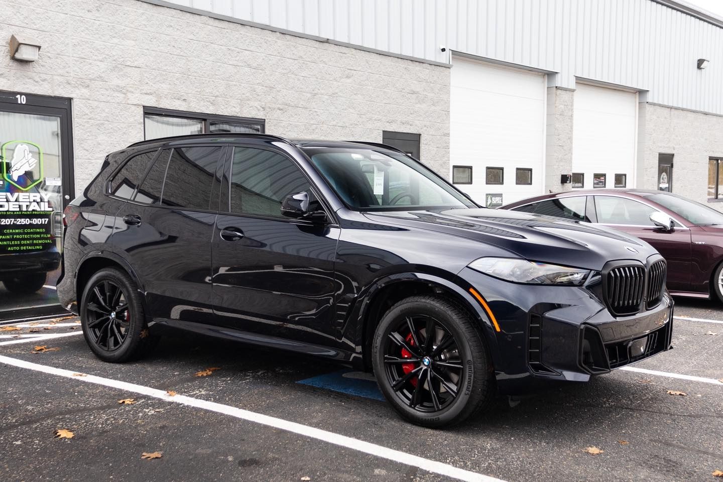 Black BMW SUV parked outside a building with garage doors. Red brake calipers visible.