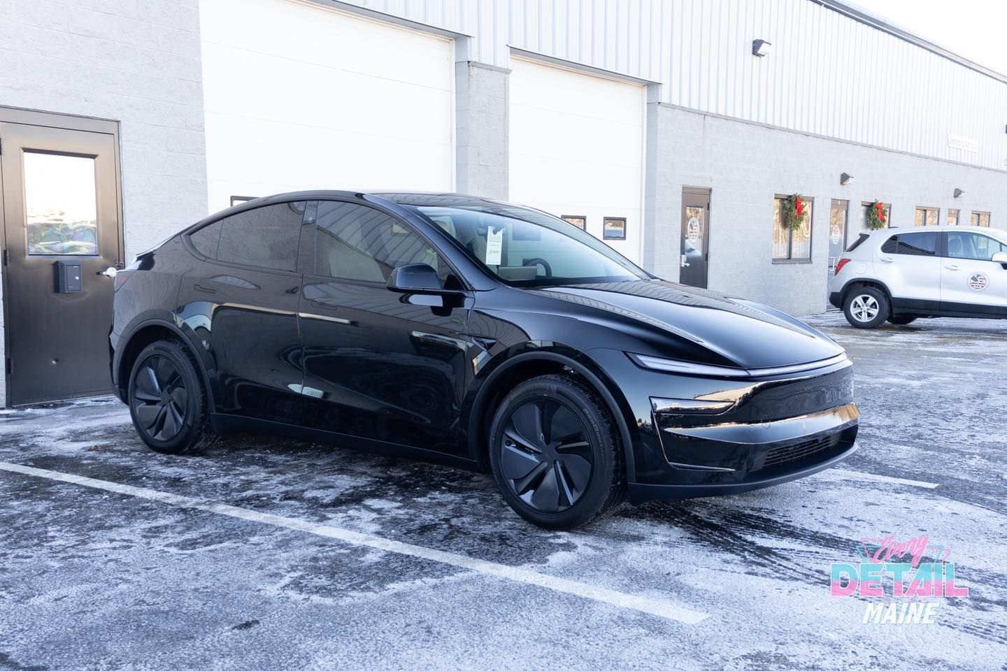 Black Tesla Model Y parked in front of a white building with snow on the ground.