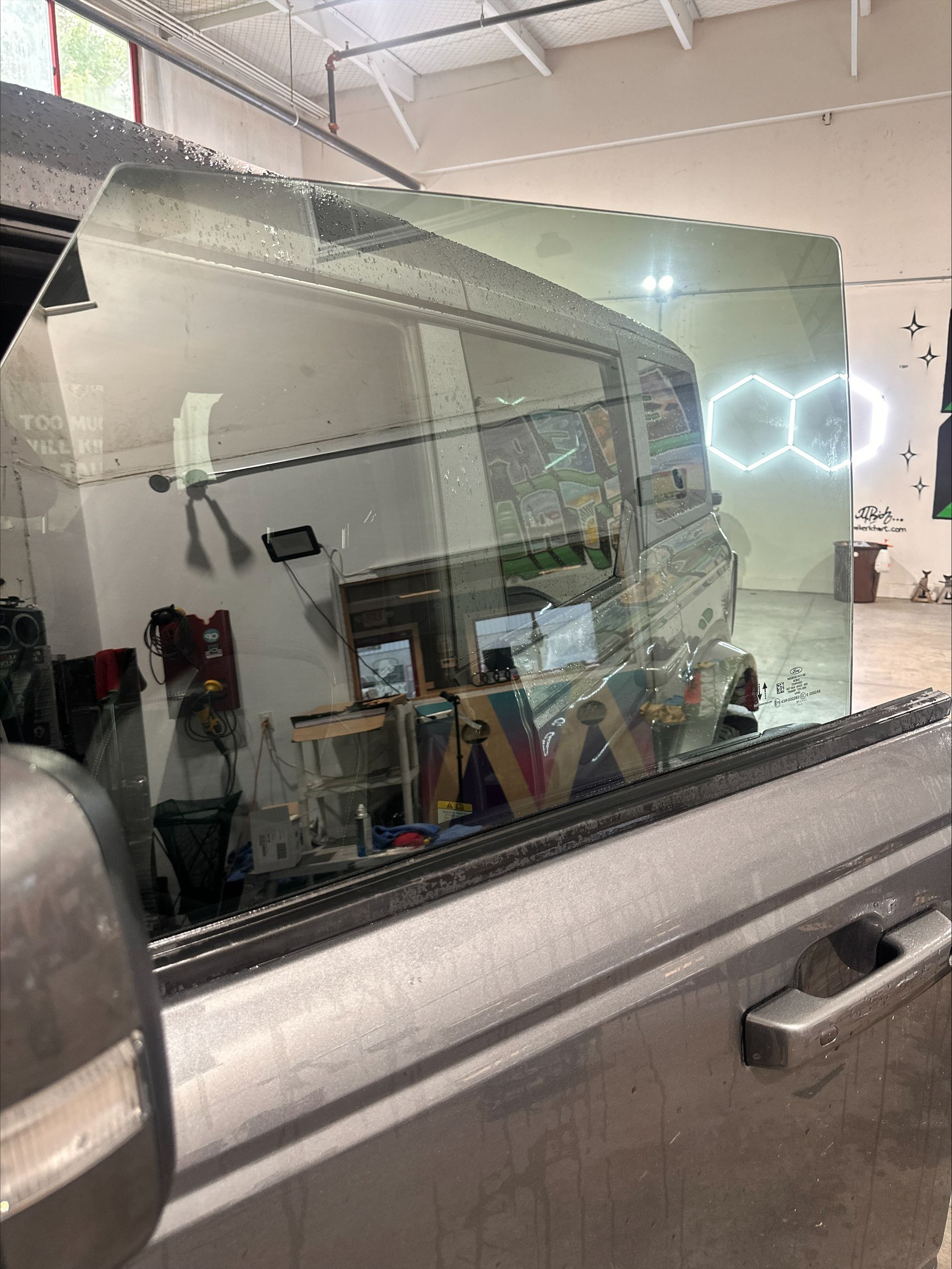 A car is parked in a garage with a reflection of a building in the window.