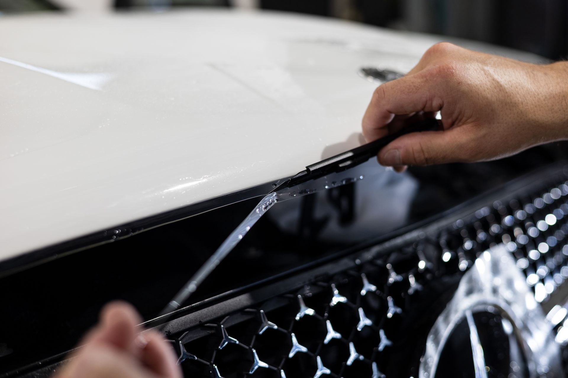 Black Mercedes convertible with protective film being applied in a garage.