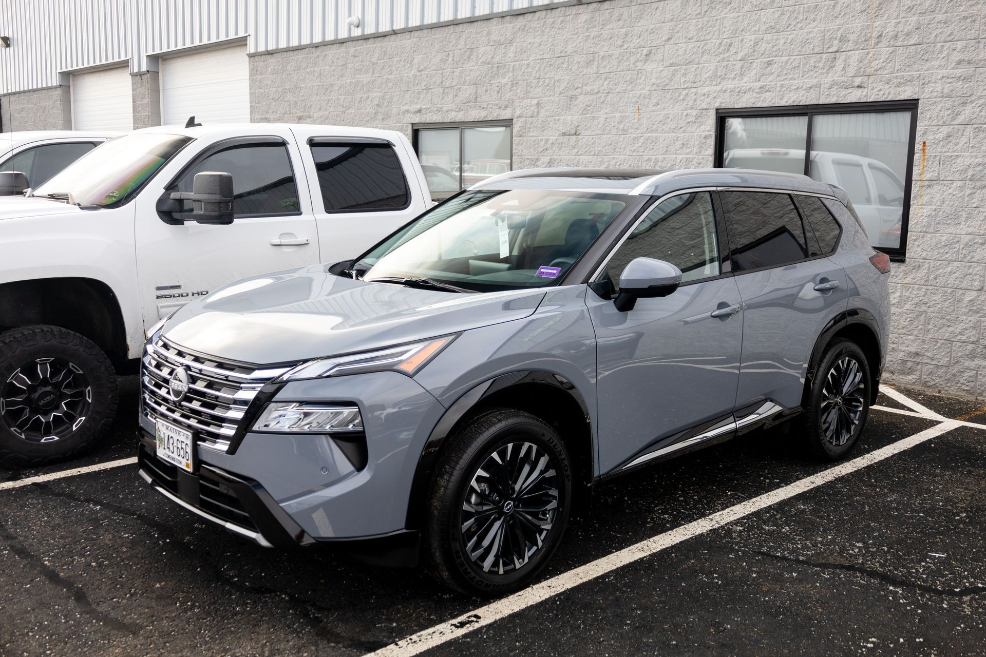 Gray Nissan Rogue SUV parked next to a white pickup truck in a paved lot near a building.