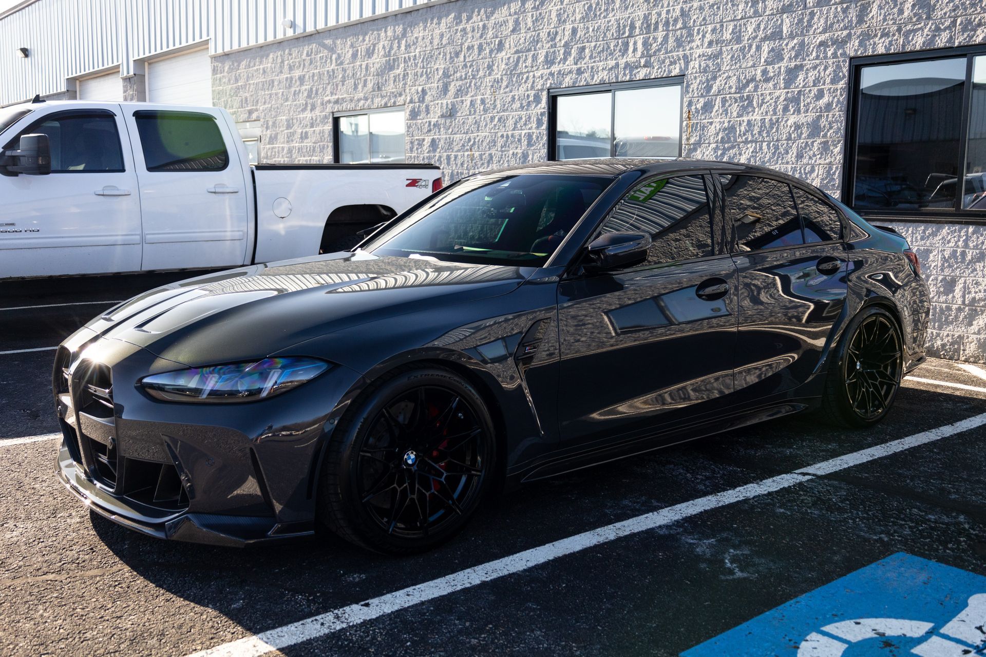 Dark gray BMW sedan parked in front of a building with black wheels and tinted windows.