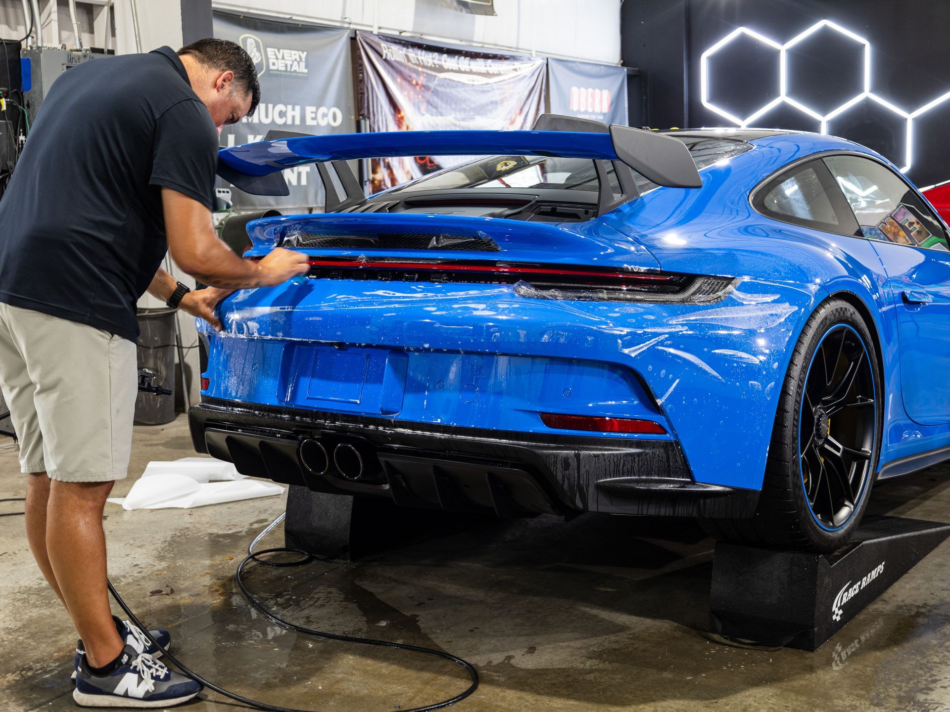 Man cleaning a bright blue Porsche sports car; garage setting.