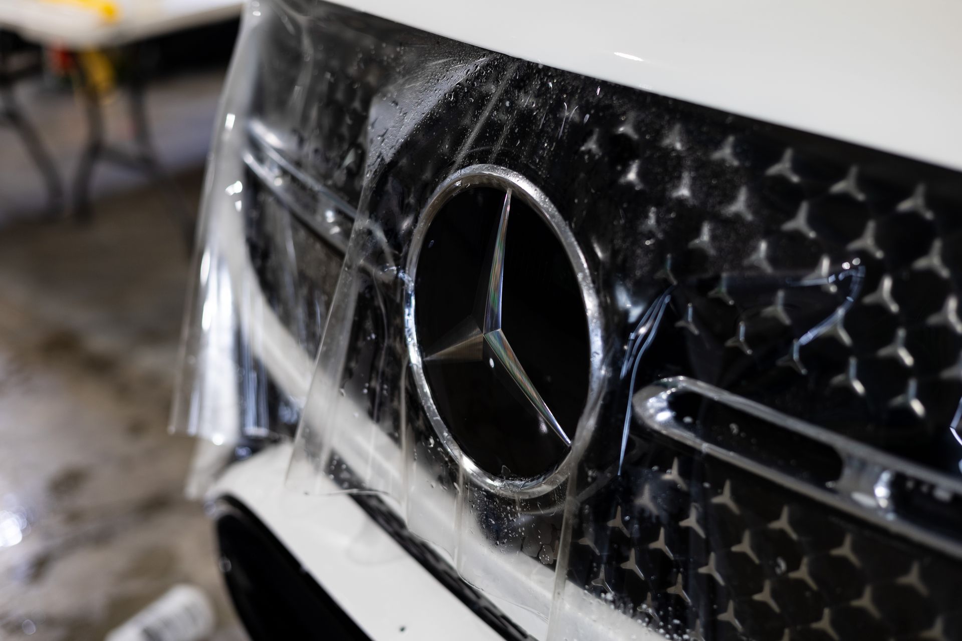 Applying clear protective film to a Mercedes-Benz grille with the iconic logo.