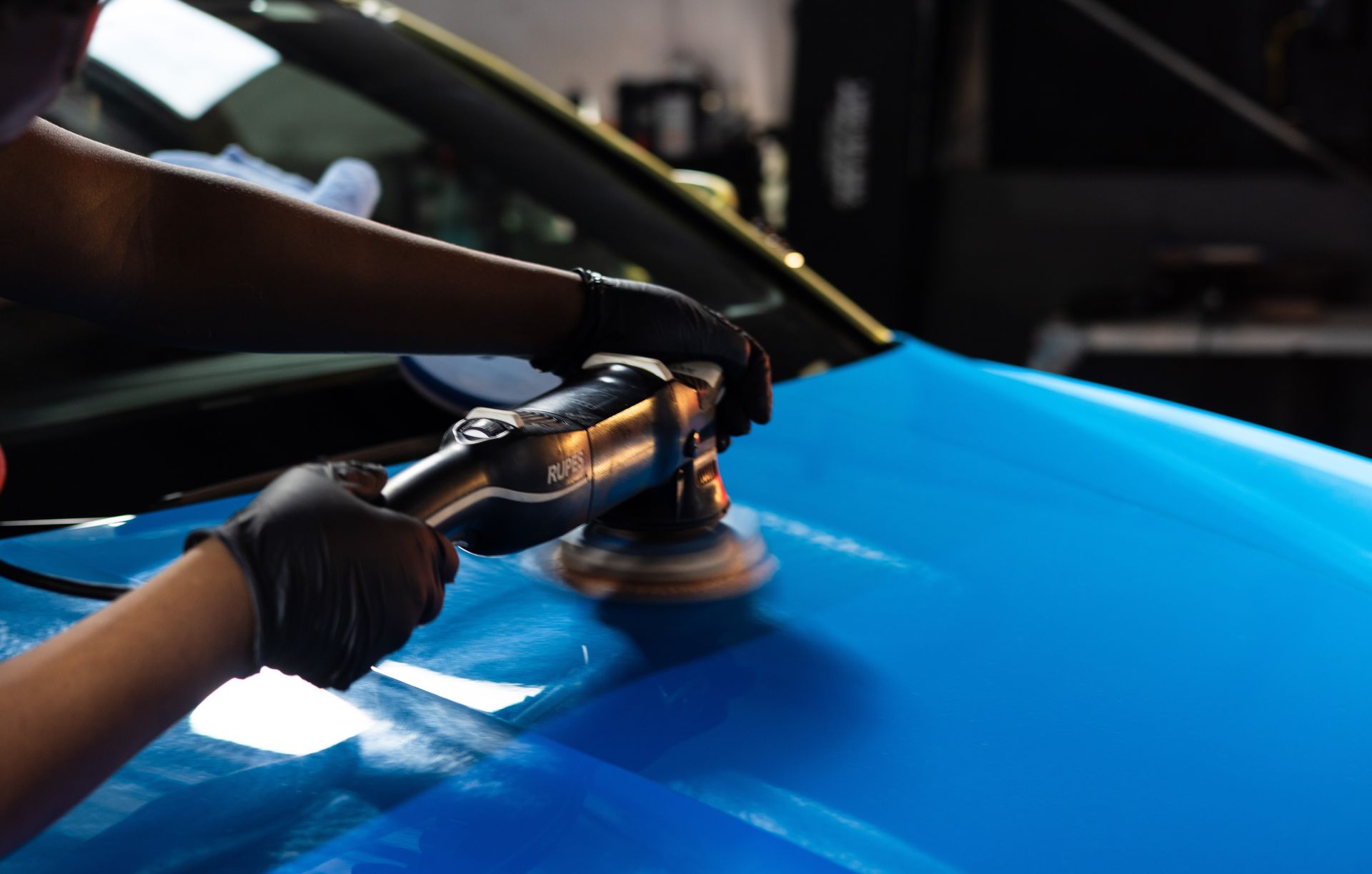 Person polishing a bright blue car with a handheld polisher.