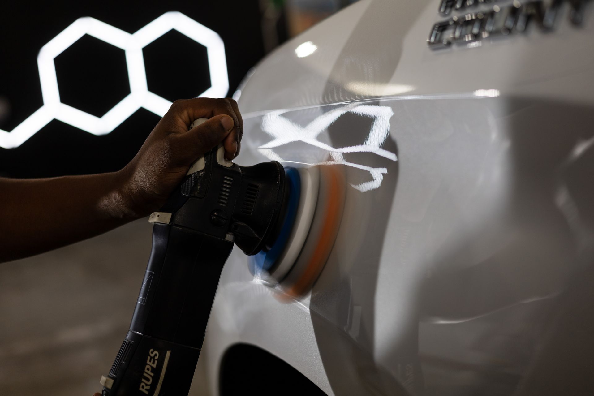 Person polishing a white car with a Rupes polisher, showing reflection.