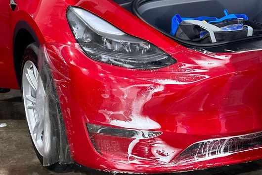 A red tesla model 3 is being washed in a car wash.