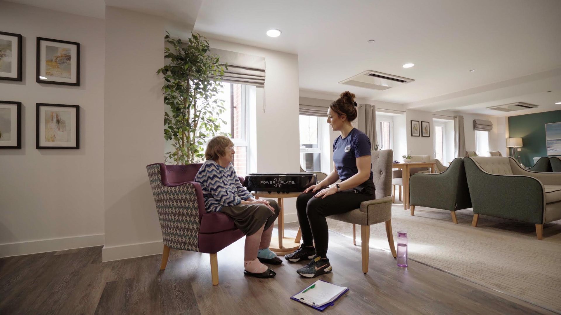 A woman is sitting in a chair talking to an older woman in a living room.