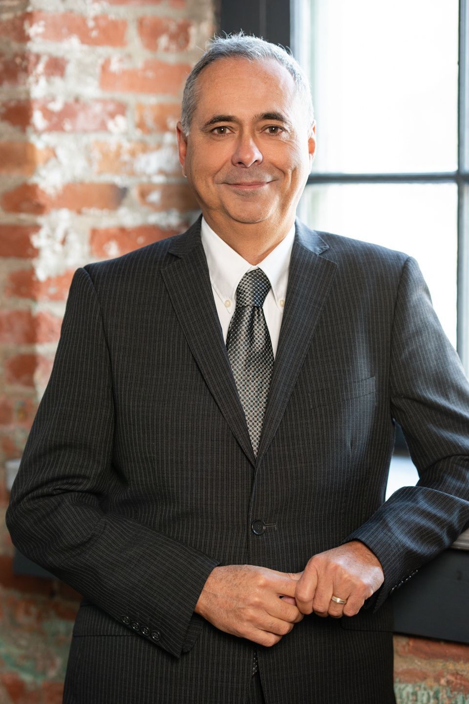 Un homme en costume et cravate se tient devant un mur de briques.