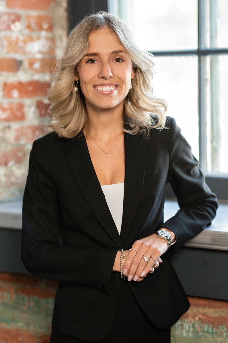 Une femme en costume noir se tient devant une fenêtre.