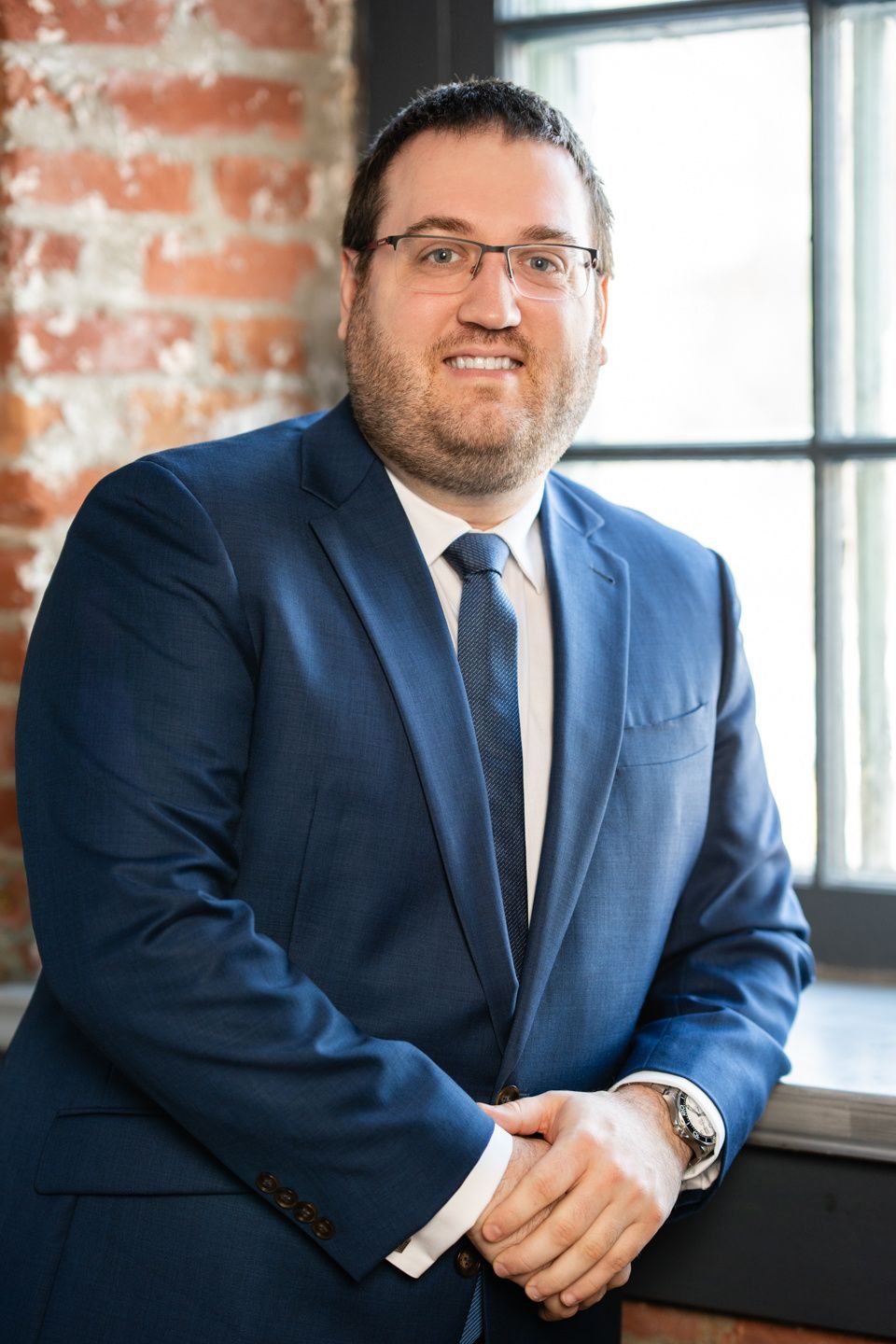 Un homme en costume et cravate se tient devant une fenêtre.