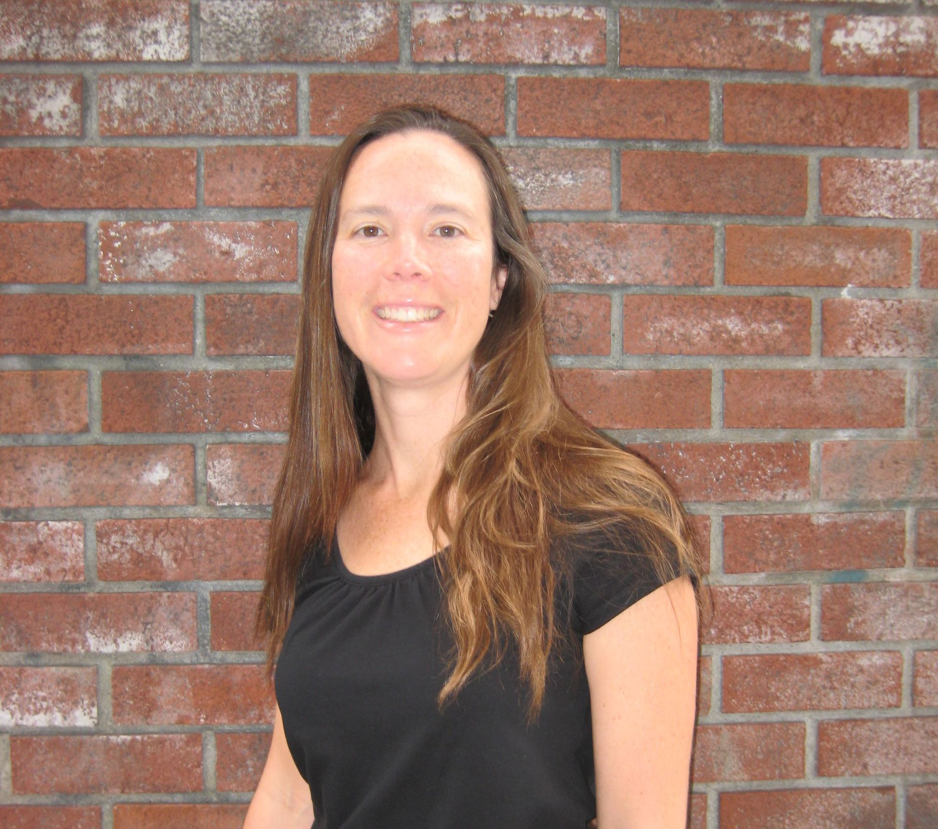A woman in a black shirt is smiling in front of a brick wall