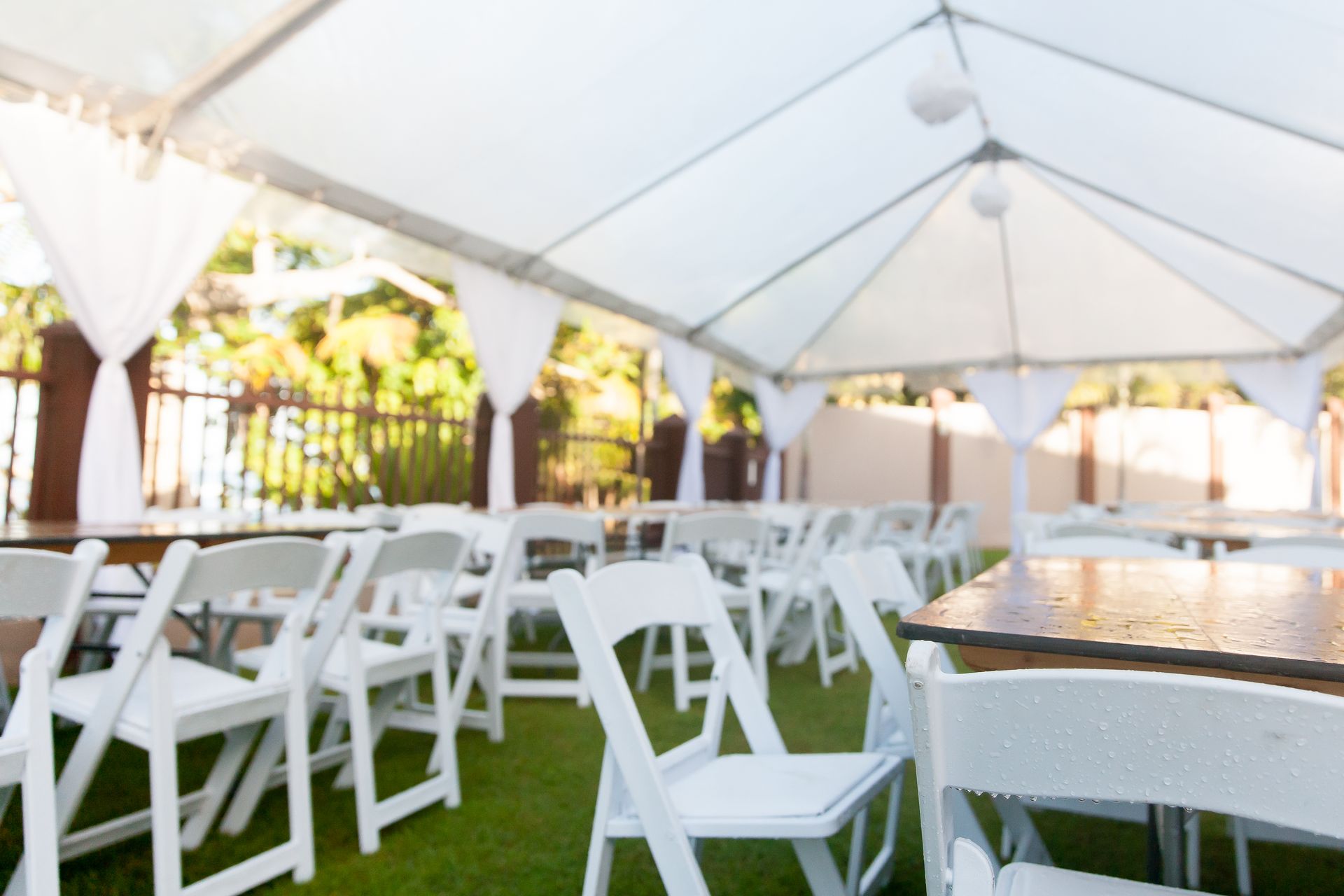 A row of white folding chairs and tables under a tent.