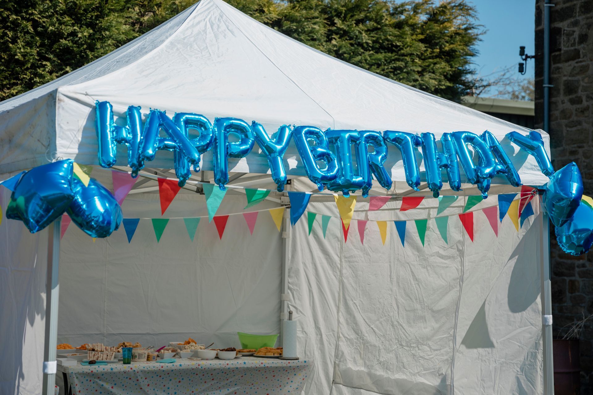 A white tent with blue balloons that say happy birthday