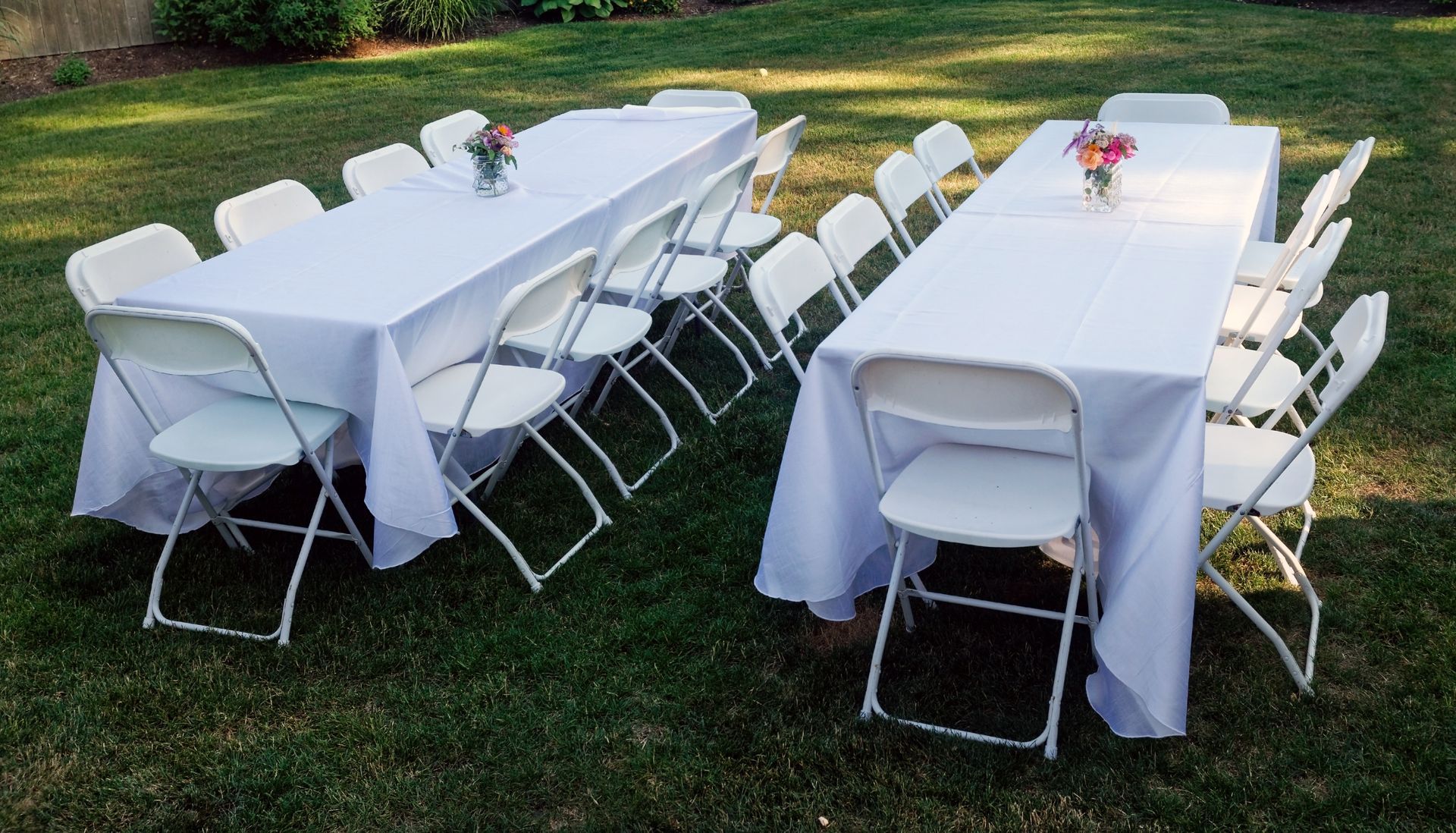 A row of folding chairs and tables in a grassy field.