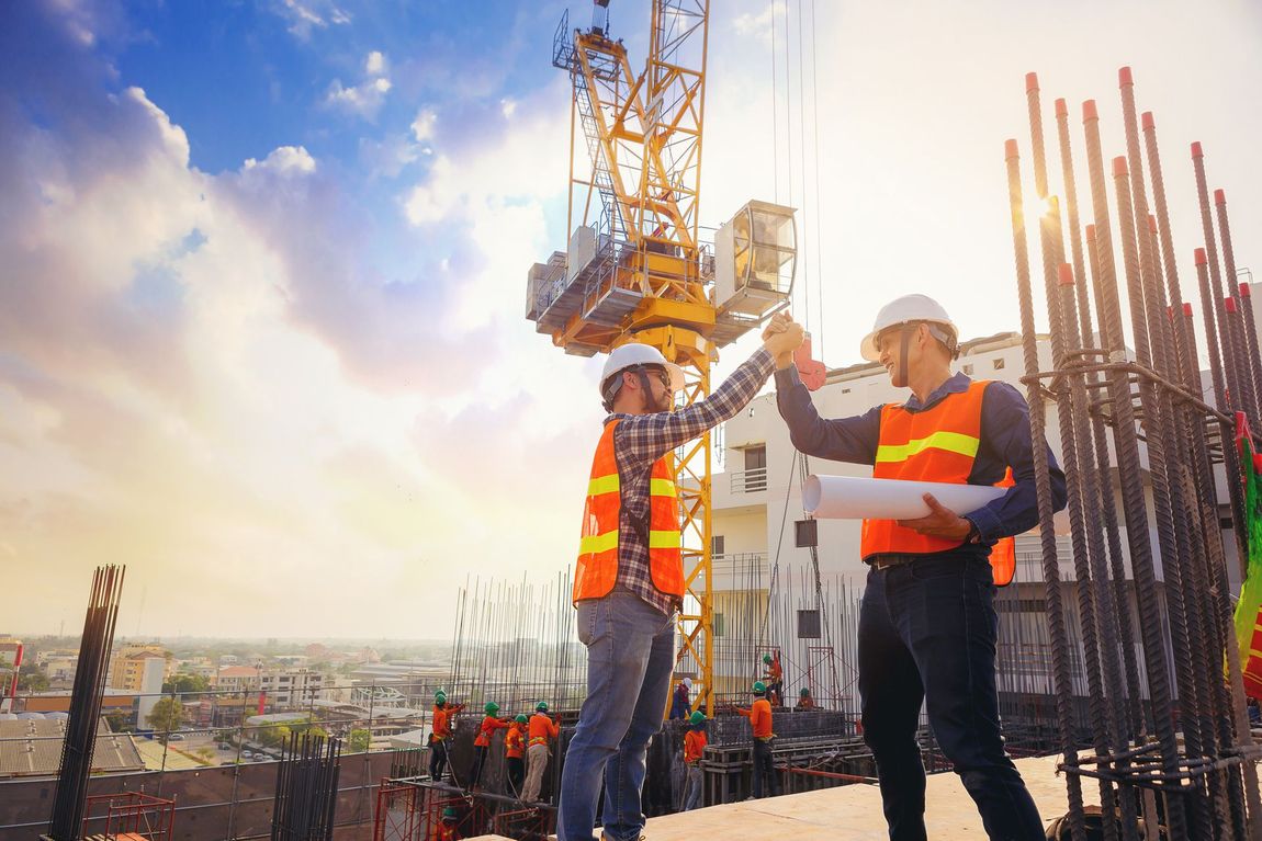 Two construction workers are shaking hands at a construction site.