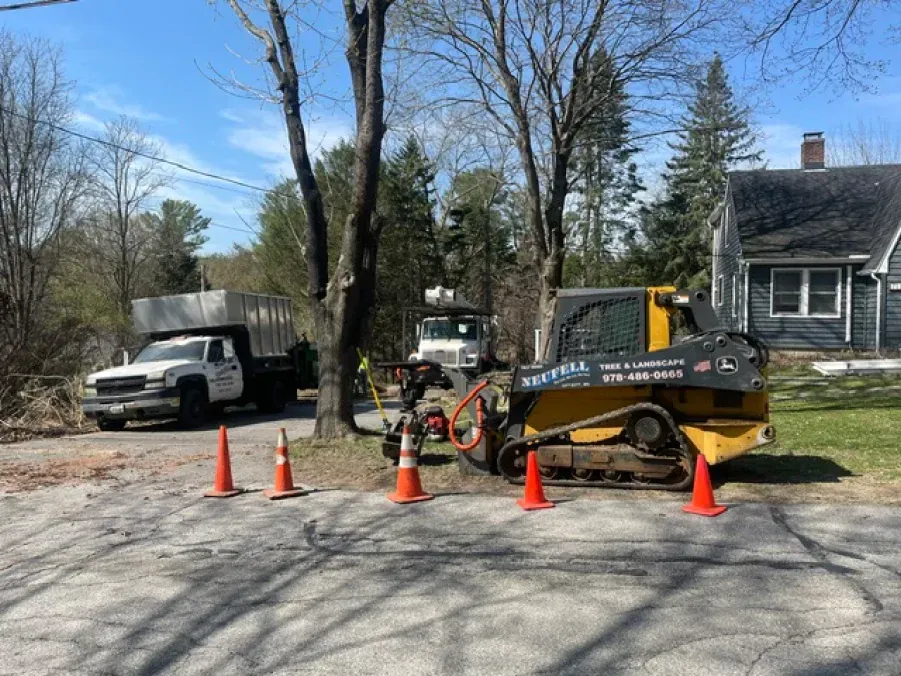 A bulldozer is parked in a driveway next to a truck and cones.