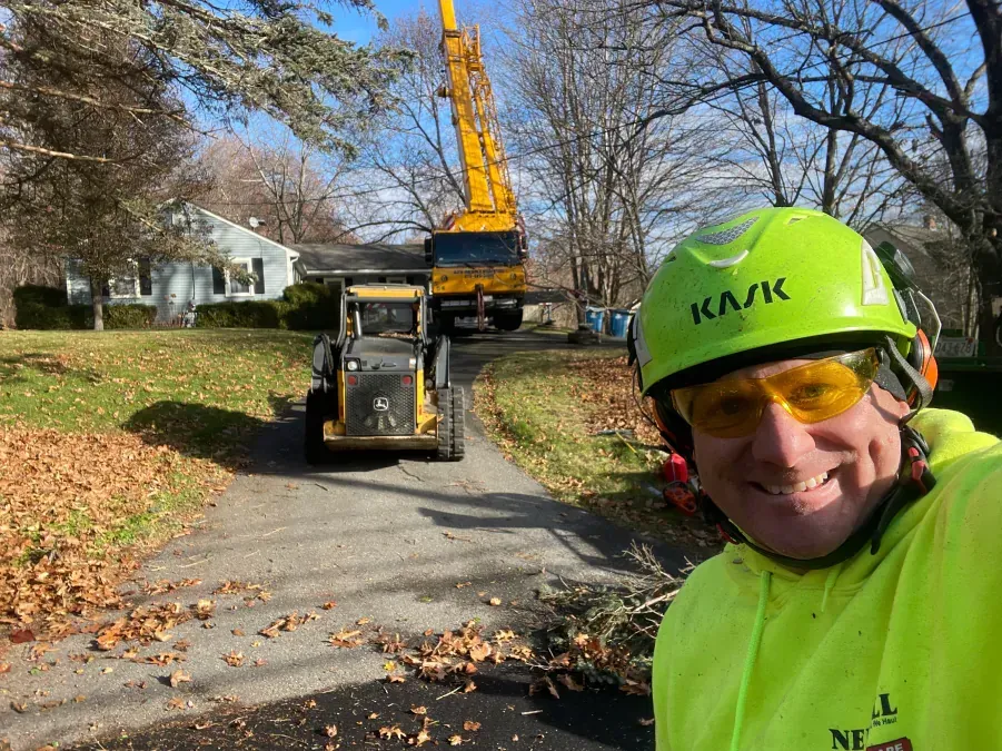 A man wearing a yellow helmet and sunglasses is taking a selfie with a crane in the background.
