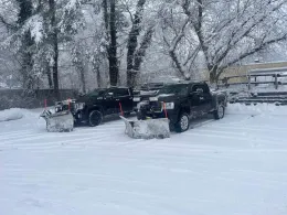 Two snow plows are parked next to each other in the snow.