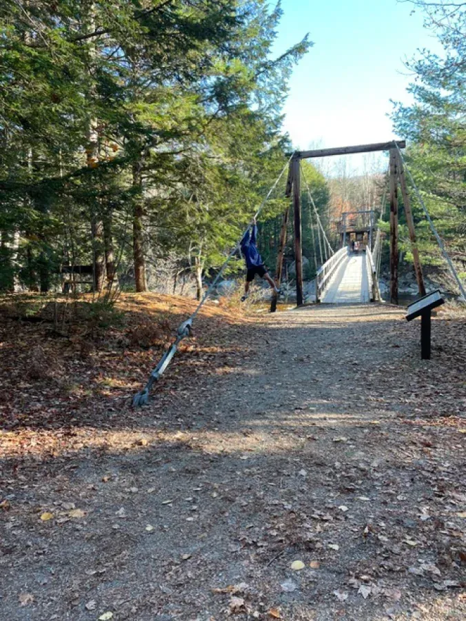 A person is riding a zip line over a bridge in the woods.