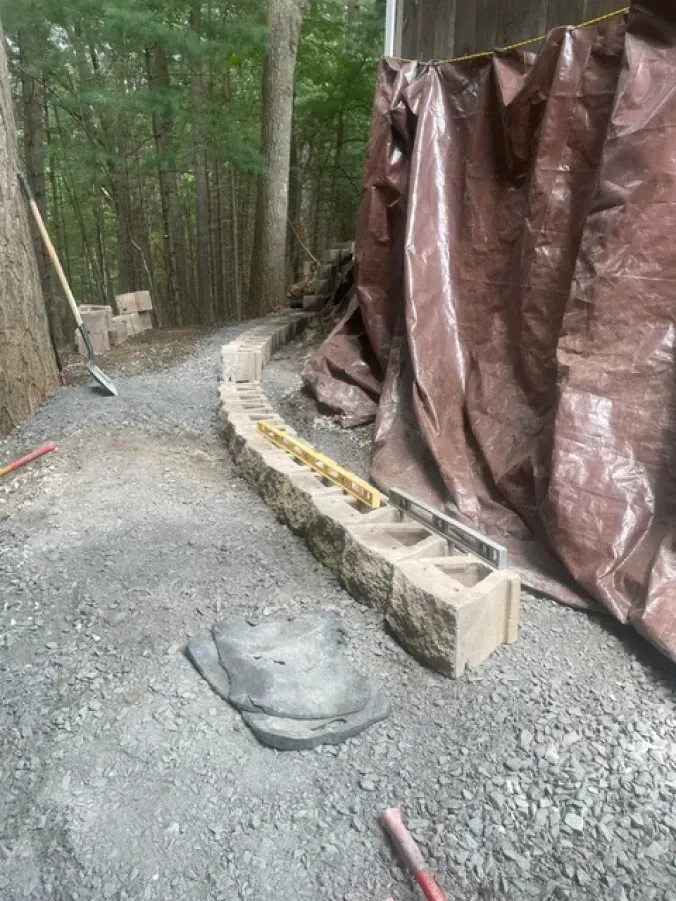 A brick wall is being built on a gravel road in the woods.