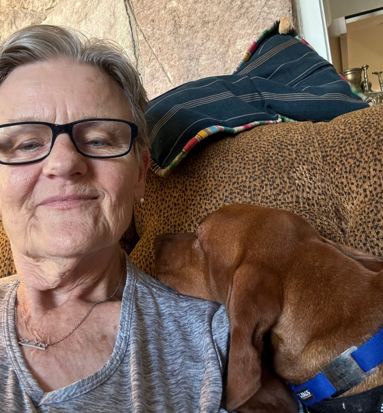 A woman wearing glasses is sitting on a couch with a brown dog.