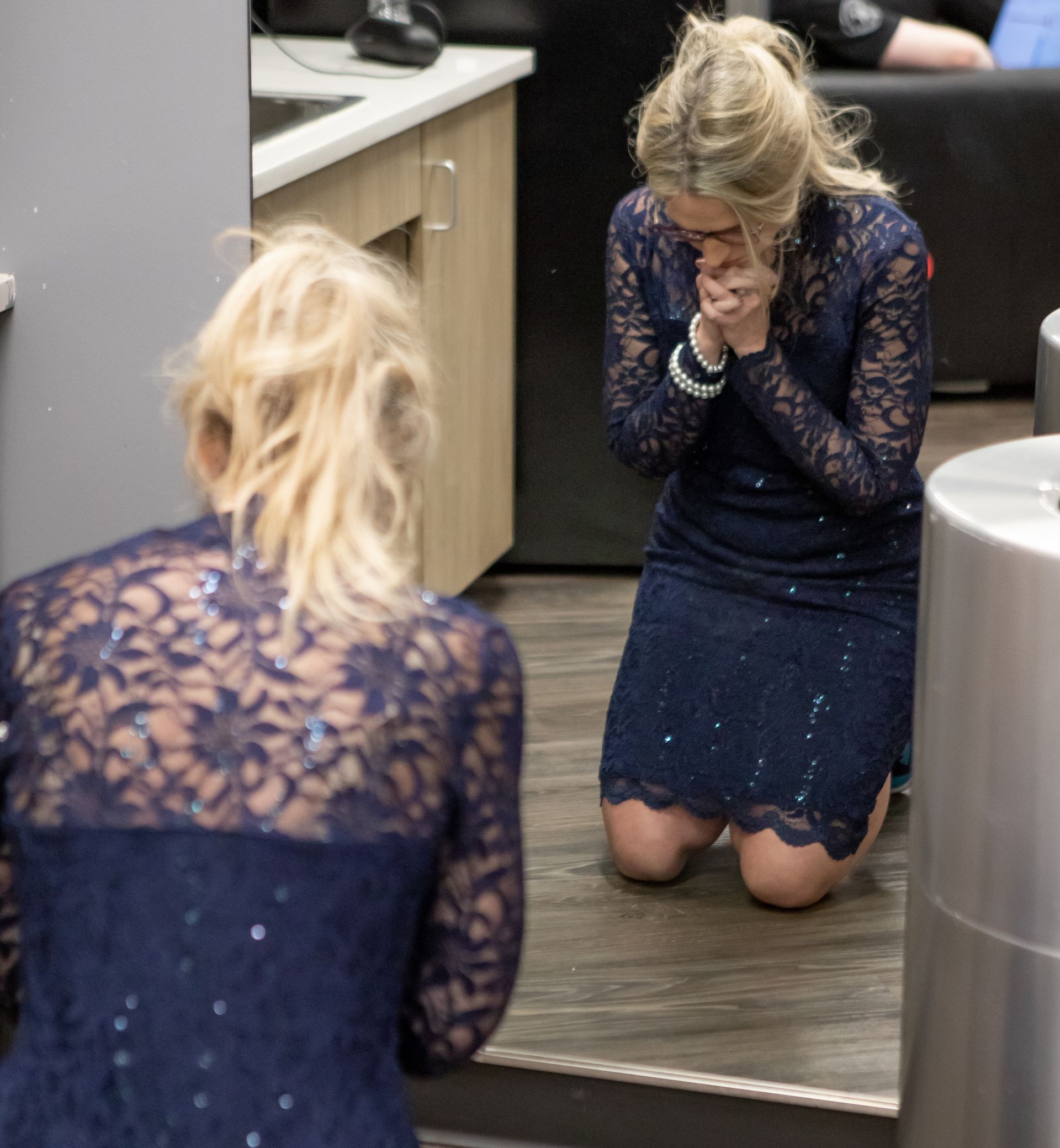 A woman in a blue dress is kneeling down in front of a mirror