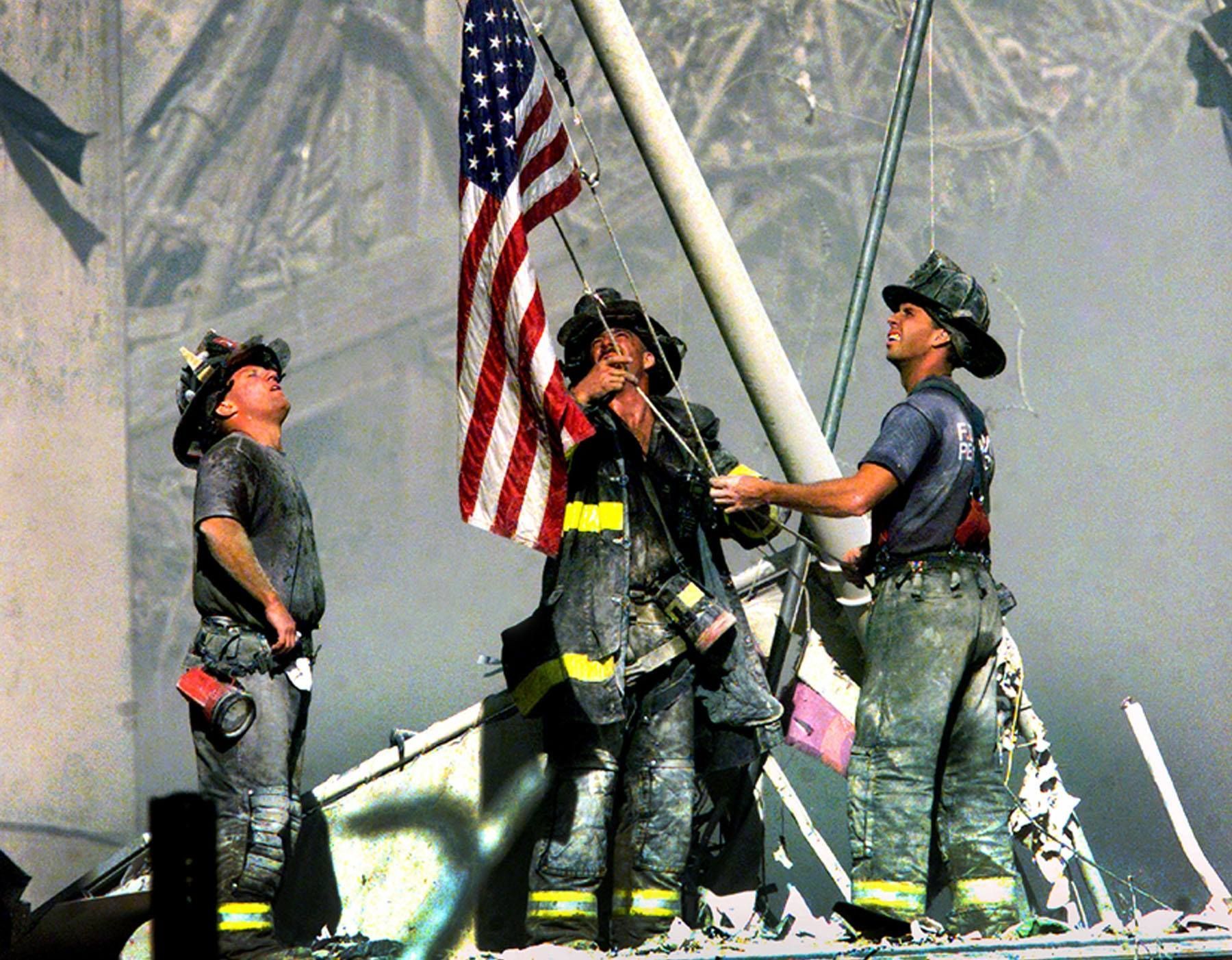 A group of firefighters are raising an american flag