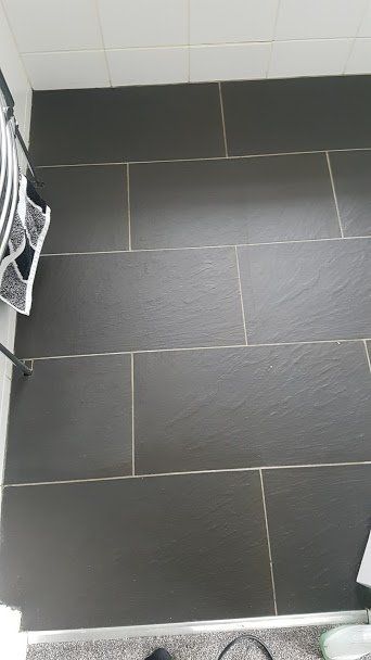 A black tile floor in a bathroom with a white wall.