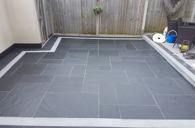 A patio with black tiles and a wooden fence in the background.