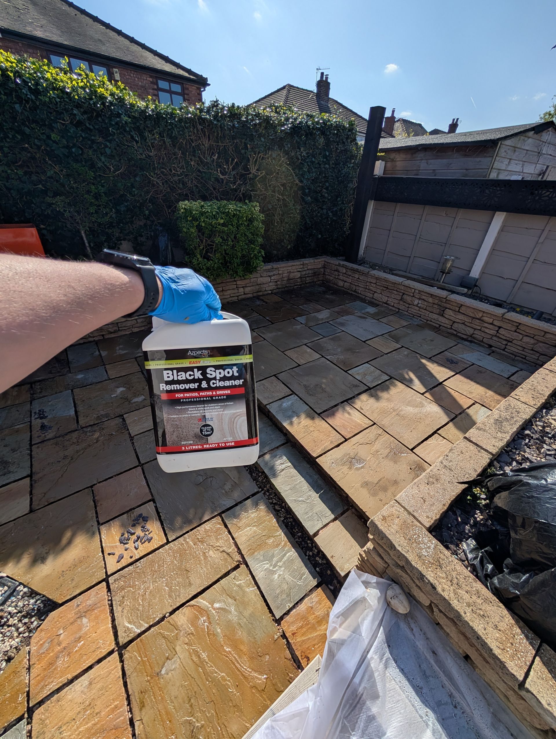 Outdoor patio tiles undergoing professional deep cleaning with one of the cleaning products used Azpects Black Spot Remover bottle in the foreground.