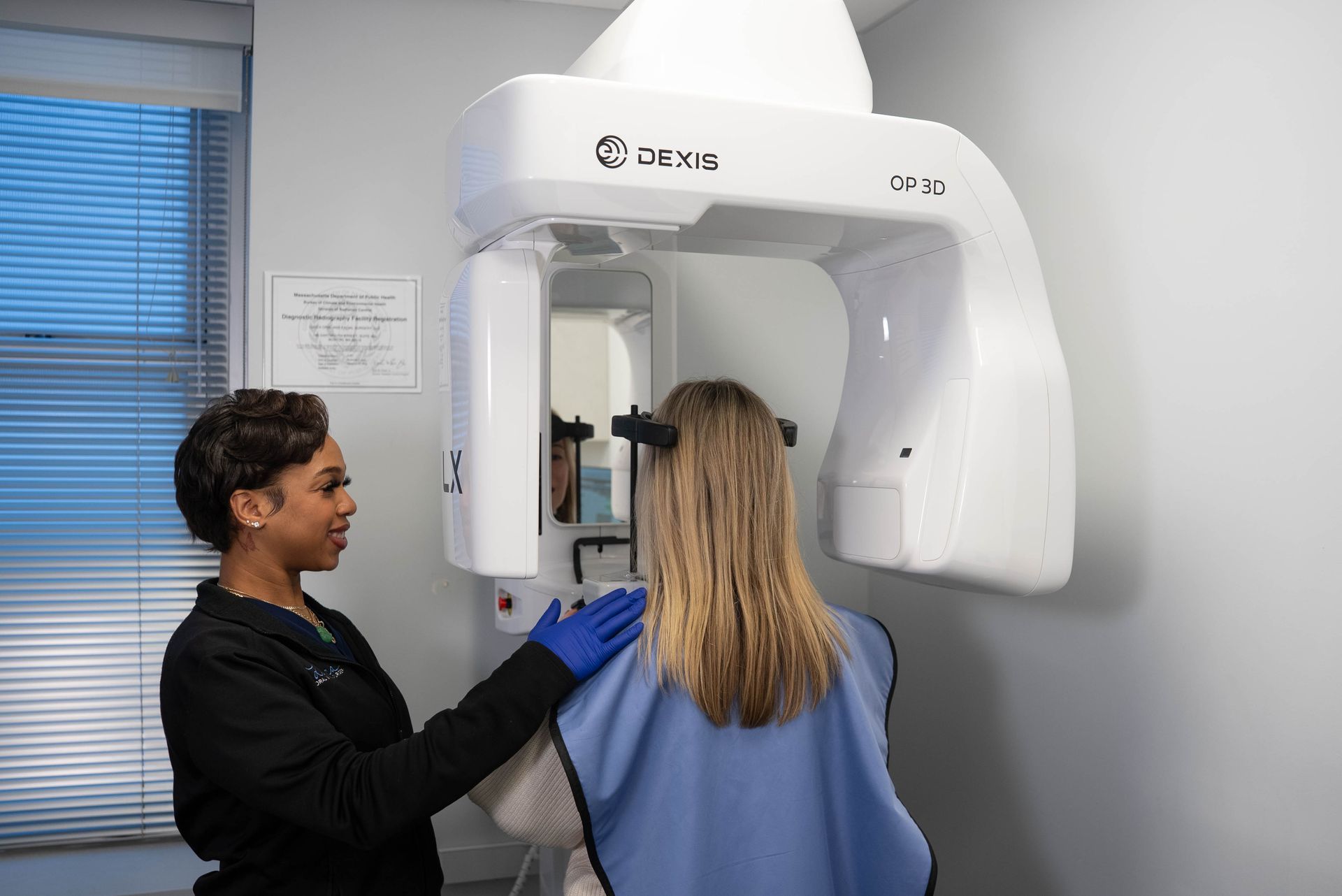 Dental assistant preparing patient for an X-ray scan using a large white imaging machine.
