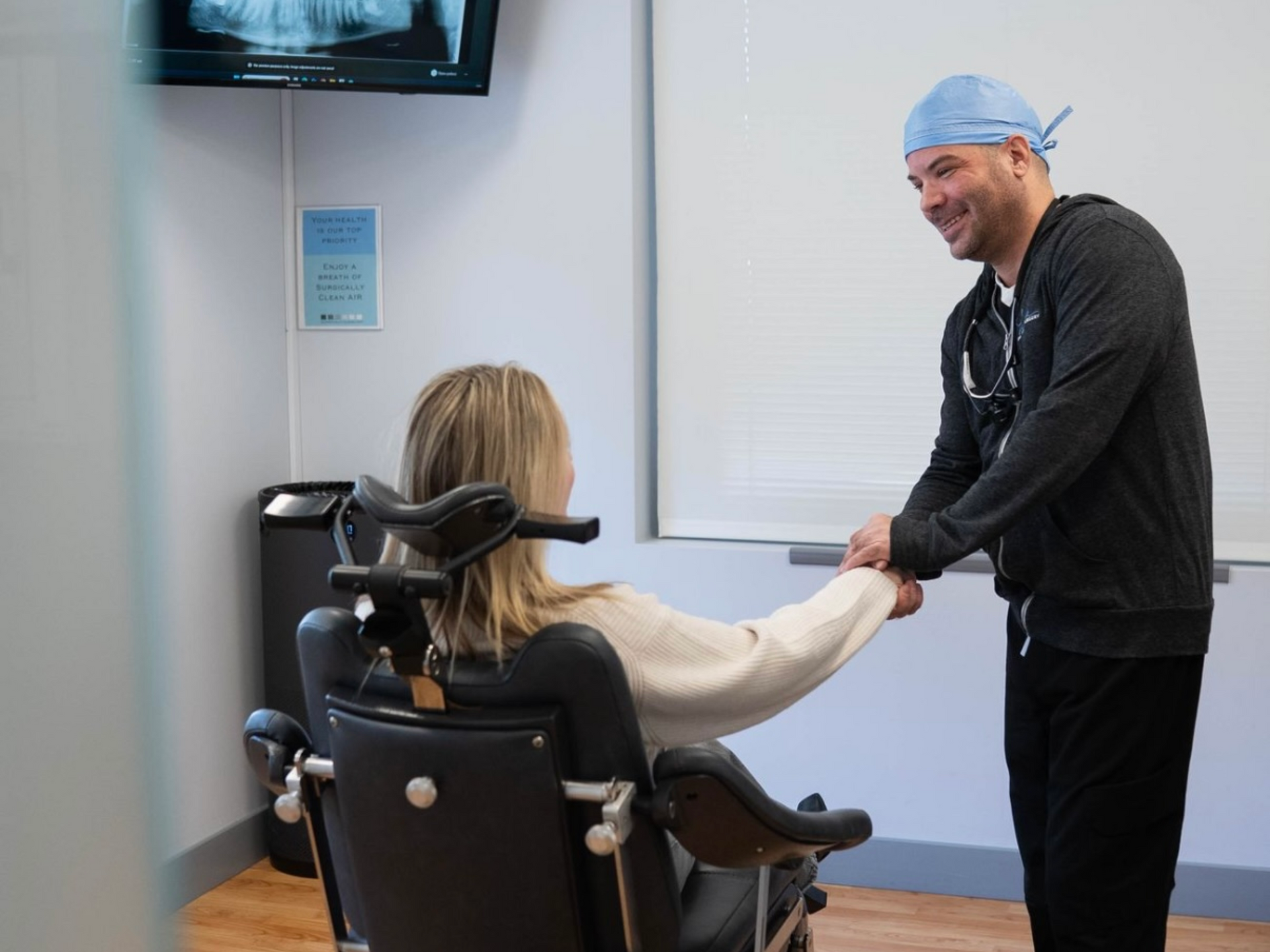 Dr. Lucca in a dental office points to a panoramic dental X-ray on a monitor for a seated patient.