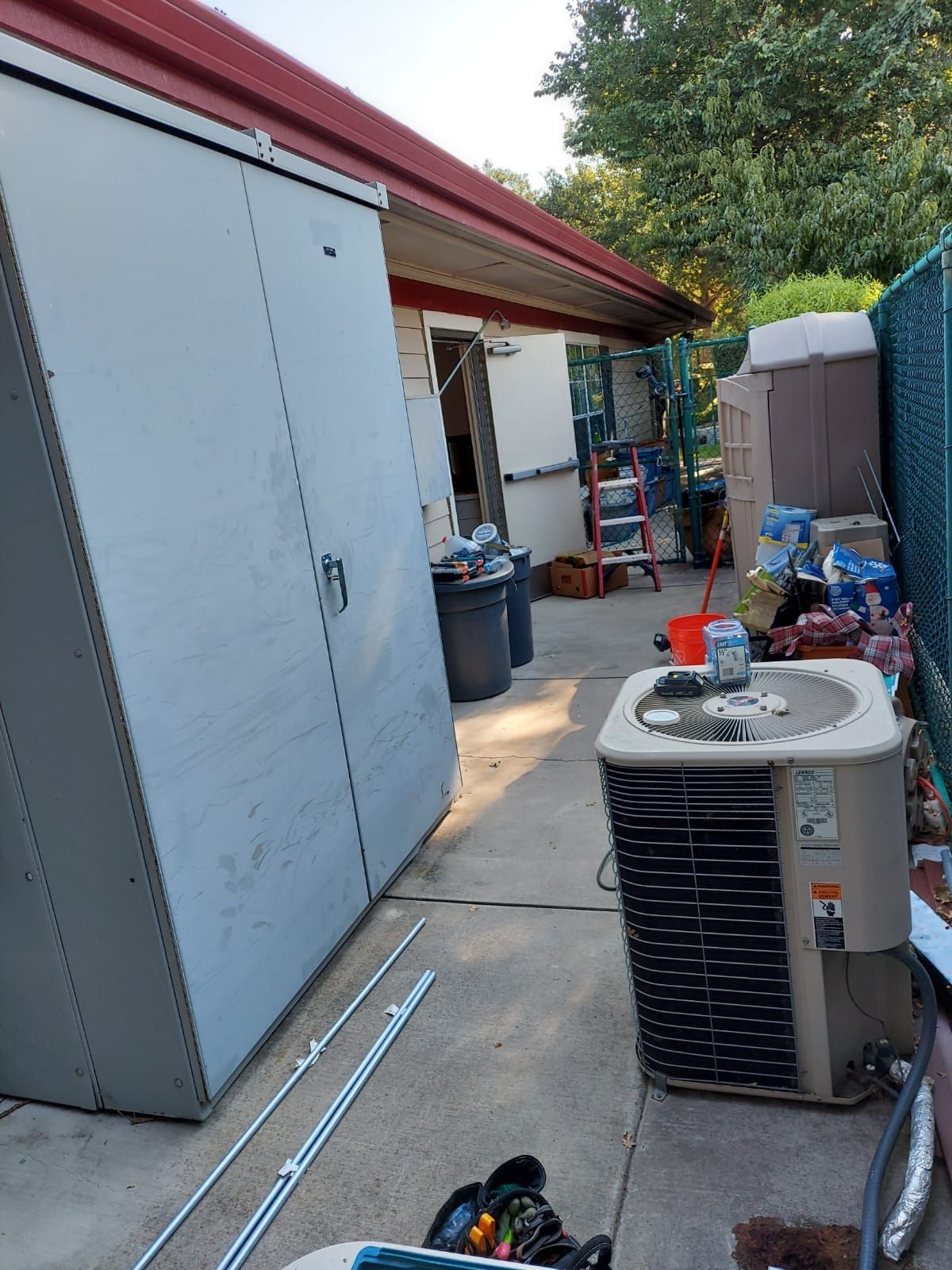 An air conditioner is sitting on the sidewalk in front of a shed.