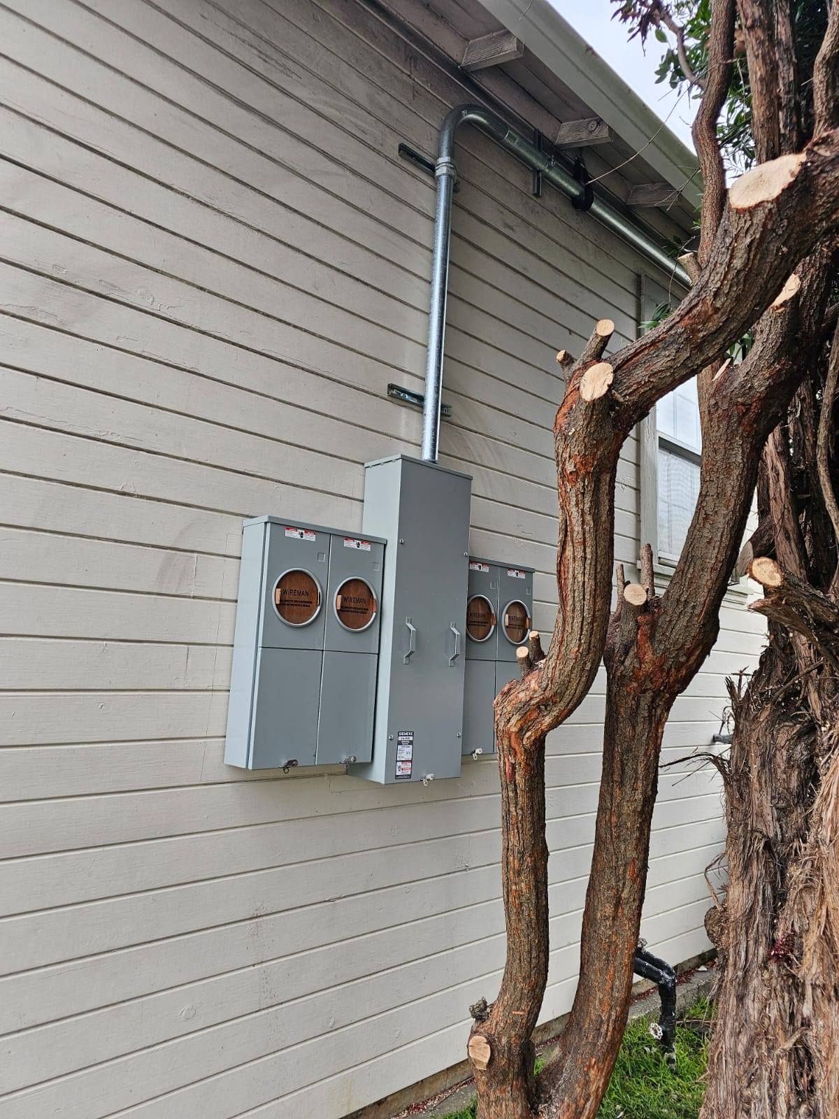 A house with a tree in front of it and electrical boxes on the side of it.