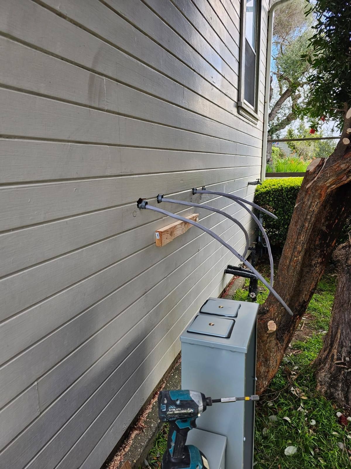 A drill is sitting on the side of a house next to a tree.