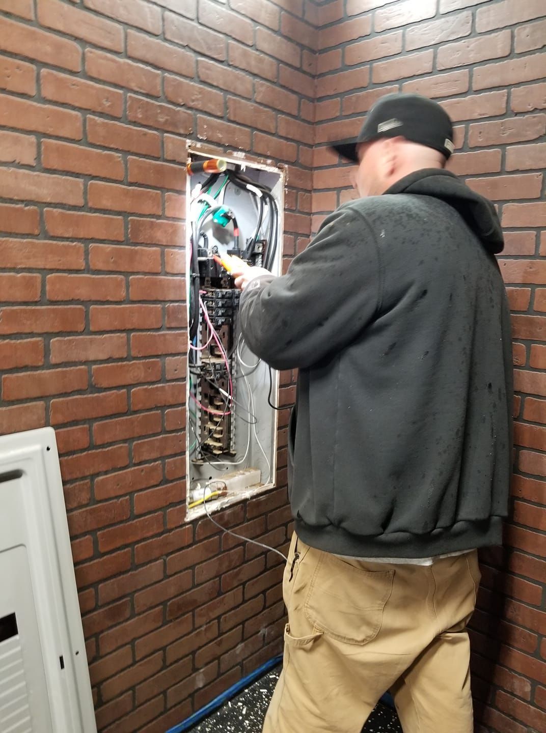 A man is working on an electrical box in a brick wall.