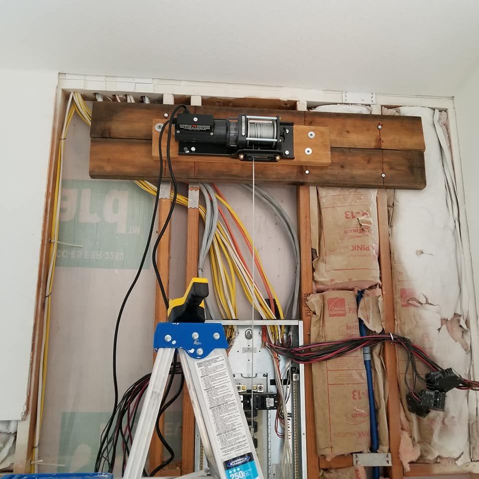 A ladder is sitting in front of a wall with electrical wires hanging from it