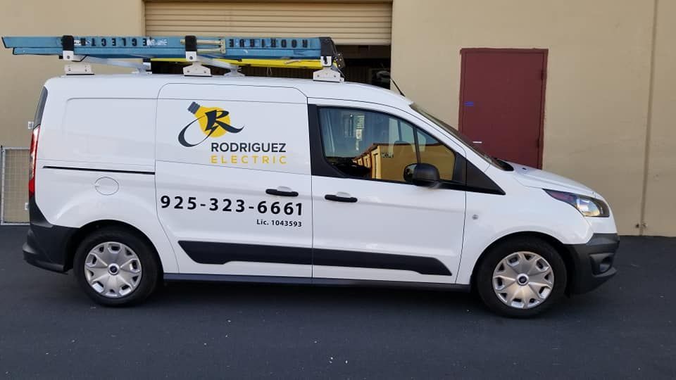 A white van for rodriguez electric is parked in front of a building