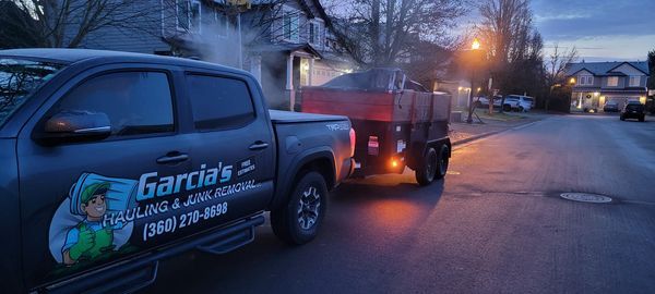 Truck and trailer on a residential street, Garcia's hauling junk. Dusk.